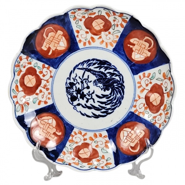 Prato circular de porcelana Imari, caldeira com ave do paraiso e borda ondeada com painéis florais intercaladas por objetos preciosos. Esmaltagem em vermelho ferro e azul cobalto. 21,5 cm diâmetro. Ja