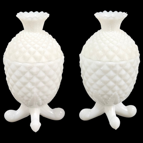 Par de caixas de opalina branca, sobre pés elevados que concluem em rocalha. Corpo bojudo decorado com elementos geométricos estilizados e repetitivos. Pega da tampa com borda recortada. 18 cm altura.