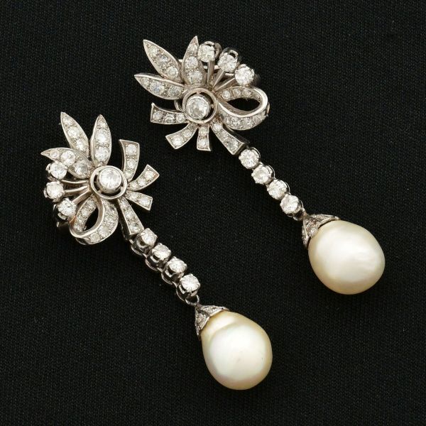 Par de brincos vintage, em platina, modelo floral, com laços e pétalas articuladas e pendentes duas tiras verticais, interligando o topo decorativo da base da joia, finalizadas com duas pérolas de apr