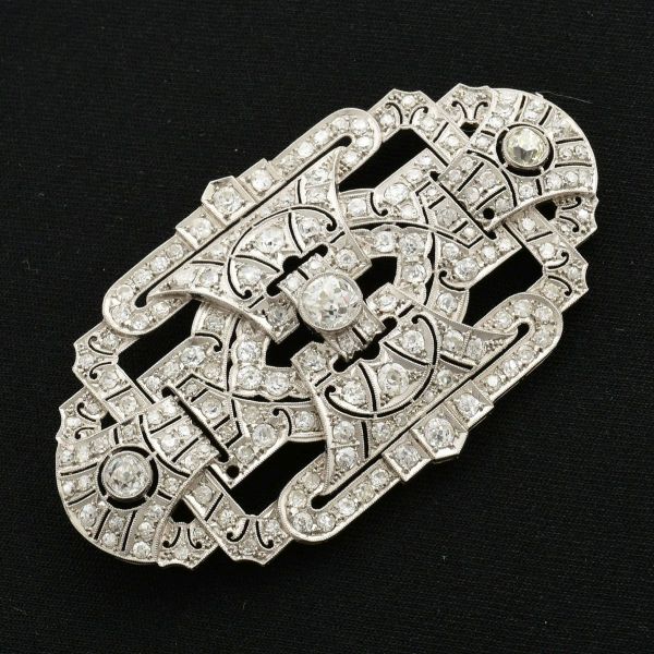 Broche art decó em platina, tendo em sua parte principal, tres diamantes, sendo o do meio com aprox 1,2 ct e dois diamantes laterais de aprox 0,33 ct cada. Broche totalmente cravejado com aproximadame