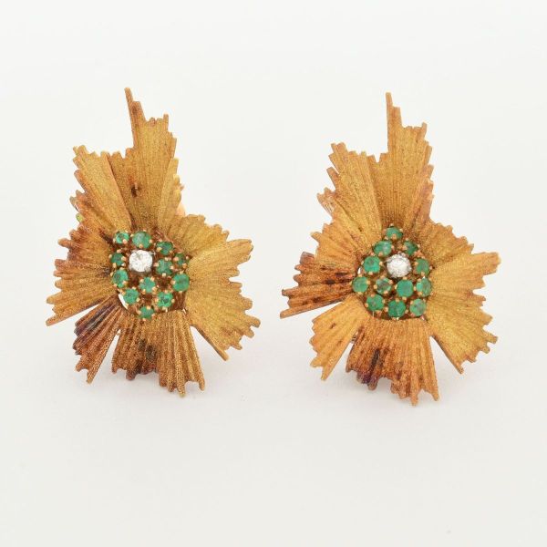 Par de brincos em ouro amarelo 18 k, em formato de flor, caracterizado com pétalas desfiadas ou texturizadas, tendo ao centro pavê de pequenas esmeraldas e dois diamantes centrais de aproximadamente 0