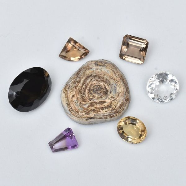Conjunto contendo sete pedras brasileiras, sendo uma em formato de fatia, em ágata, tres pedras provavelmente citrinos, uma ametista, um quartzo fumê lapidado e uma gema transparente e lapidada. Peso