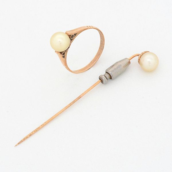 Conjunto em ouro amarelo 18 k, sendo um alfinete de gravata com pérola de 7,3 mm, medind0 6,5 cm de comprimento e um anel, aro 21, com pérola de 7,4 mm. Peso total 5,2 g.