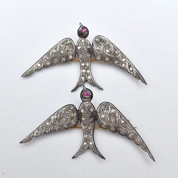 Par de broches em ouro branco e amarelo, em formato de andorinhas, cravejadas de pequenos diamantes e olhos em rubis. Medida: 4,7 x 2,6 cm. Peso total 9,4 g.