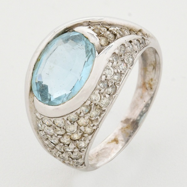 Anel em ouro branco 18 k, abaulado, com pedra azul central em tom azul claro, de um lado, decorada com mini pedras brancas e do outro, trabalhos vazados em formato de estrelas. Aro 14/15. Peso total 6