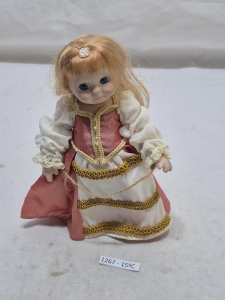 Boneca vintage de porcelana de personagem feminina em traje de época, com vestido adornado em dourado e cabelos loiros presos por uma tiara de pérolas. Medindo 18cm de altura.
