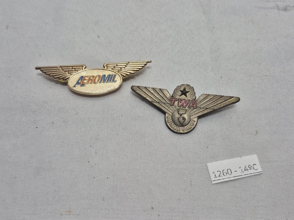 Conjunto de dois distintivos de asas de aviação, sendo um da companhia AEROMIL em metal dourado com fecho duplo tipo pin e outro da TWA (Trans World Airlines) Junior Pilot em metal prateado com fecho
