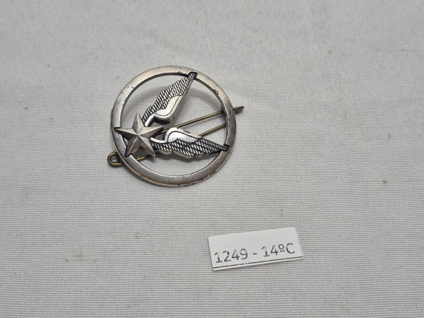 Insígnia metálica francesa de aviação militar, produzida pela tradicional fabricante Drago (Paris). O distintivo apresenta estrela com asas em relevo dentro de um círculo, símbolo utilizado pela Força