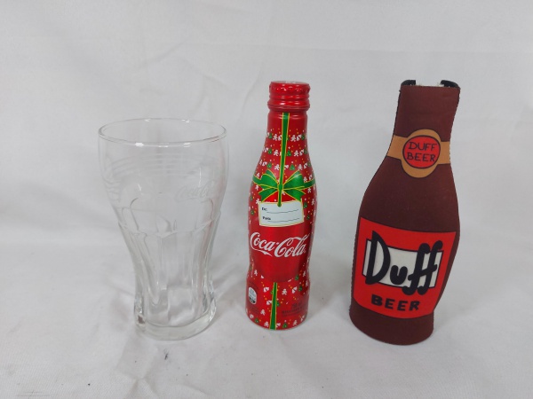 Lote de tulipa da Coca-Cola, garrafa lacrada da coca Cola e capa de garrafa da cerveja Duff. Medindo 8,5cm x 15,5cm de altura.