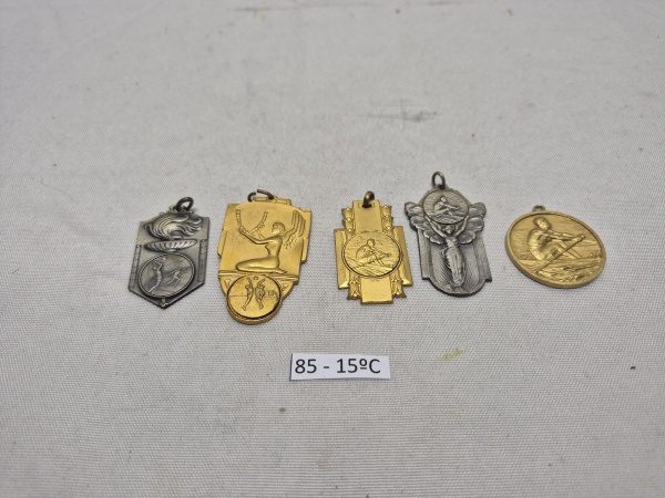 Conjunto de 5 medalhas esportivas em metal, incluindo peças em relevo representando natação, remo e voleibol, com destaque para medalha da F.A.E. datada de 1959 e insígnia da Arqui Poli. Medindo o mai