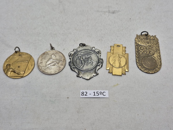Conjunto de 5 medalhas e insígnias esportivas em metal, incluindo peças em relevo representando modalidades como tênis de mesa, remo e voleibol, além de medalha comemorativa com os anéis olímpicos. Me