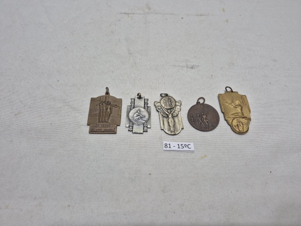 Conjunto de 5 medalhas e pingentes esportivos antigos em metal, com destaque para insígnias de remo, natação e provas clássicas, apresentando relevos detalhados e argolas para fixação. Medindo o maior