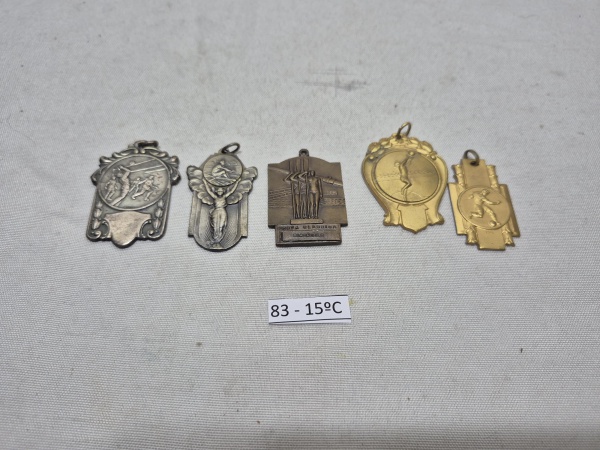 Conjunto de 5 medalhas e pingentes esportivos antigos em metal, incluindo insígnias de voleibol, remo e atletismo, com destaque para peça da Prova Clássica Riachuelo e relevos detalhados de época. Med