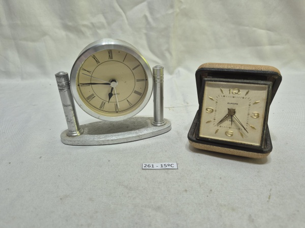 Conjunto de 2 relógios de mesa vintage, sendo um modelo Quartz em metal prateado com algarismos romanos e um relógio de viagem Europa de 2 rubis em estojo dobrável. Medindo o maior 10cm de altura. Não