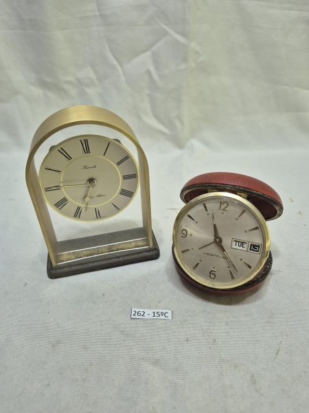 Conjunto de 2 relógios de mesa vintage, sendo um modelo Kienzle com mostrador suspenso em arco dourado e algarismos romanos, e um relógio de viagem Westclox com mostrador de dia e data em estojo circu