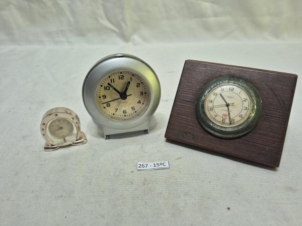 Conjunto com 3 relógios de mesa, incluindo um despertador quartz prata, um mini relógio dourado e um relógio Kienzle em suporte de madeira. Medindo o maior 10cm de diâmetro. Não testado.