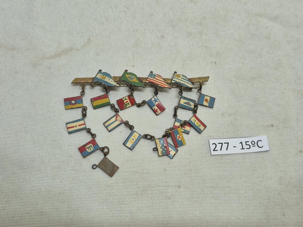Antigo broche de metal com temática náutica apresentando 4 bandeiras de países no topo e 15 pequenas bandeiras de sinalização marítima pendentes em correntes. Medindo 7cm de comprimento.