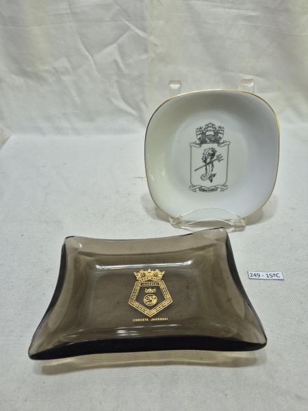 Conjunto militar composto por 2 peças, sendo um pratinho de porcelana branca com o brasão da Corbeta Guerrico e um cinzeiro de vidro fumê com o brasão dourado da Corveta Jaceguai. Medindo o maior 16cm