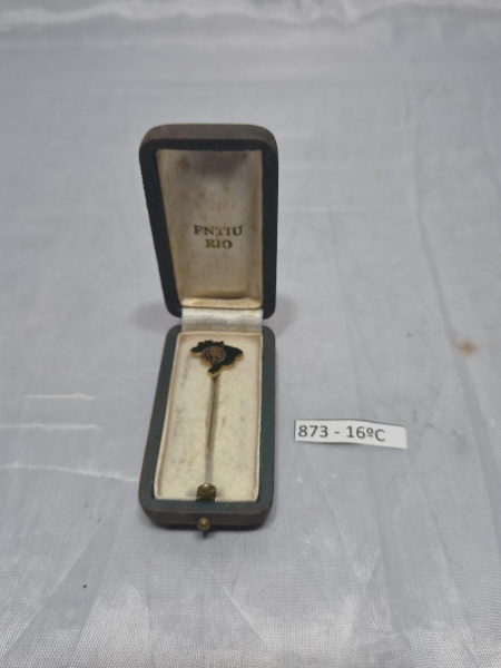 Antigo alfinete de lapela em metal dourado e esmalte verde no formato do mapa do Brasil com emblema central, acondicionado em estojo estofado de época. Medindo 4,5cm de comprimento.