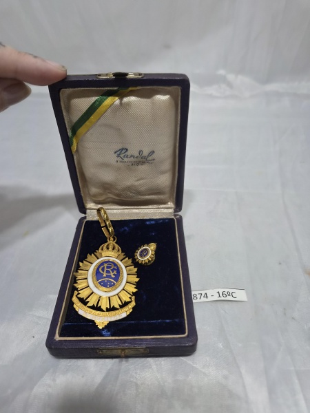 Rara medalha e insígnia de lapela em metal dourado e esmalte da Imperial Irmandade de Nossa Senhora da Glória do Outeiro, acondicionadas em estojo original de época da renomada joalheria Randal (Rio d