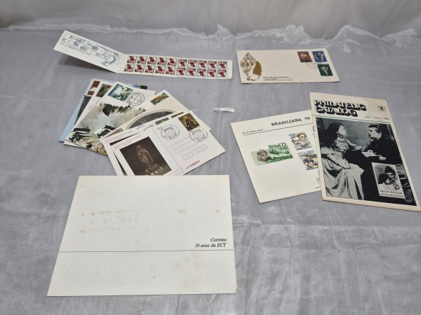 Lote variado de artigos filatélicos e postais, incluindo bloco de selos postais, envelope de Primeiro Dia de Circulação (FDC), cartões-postais comemorativos, folheto da exposição Brasiliana 79, catálo