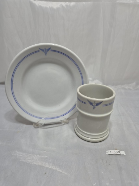 Conjunto de prato e copo em porcelana branca Rio Branco com decoração de frisos azuis e insígnia da Força Aérea Brasileira (FAB). Medindo o prato 18cm de diâmetro, copo 7,5cm x 10cm de altura
