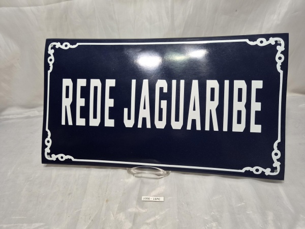 Placa metálica decorativa em tom azul escuro com moldura ornamentada e inscrição em branco "Rede Jaguaribe", com furações nos cantos para fixação. Medindo 45cm x 25cm