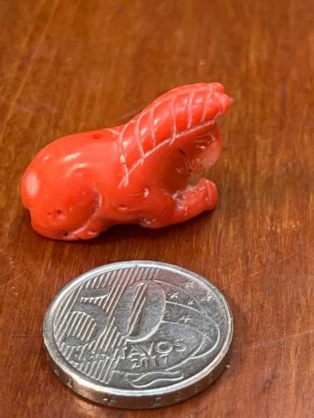 Miniatura esculpida representa um cavalo deitado (ou reclinado) feito de coral vermelho, um material orgânico muito valorizado na produção de joias antigas, amuletos e esculturas orientais de pequeno