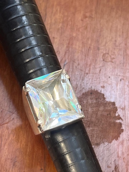 Anel solitário masculino imponente de estilo retrô. Ele apresenta uma estrutura em prata de leique segura uma grande pedra transparente de lapidação quadrada. Aro 14.