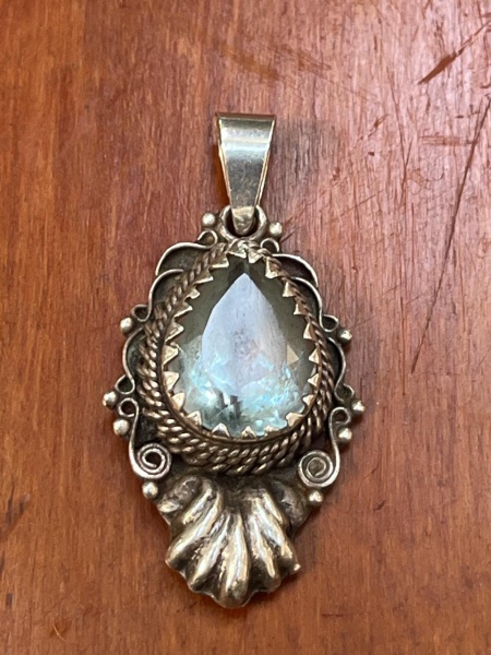 Pingente artesanal de prata de lei decorado com uma pedra natural facetada em formato de gota. O design apresenta detalhes ornamentados típicos da joalheria boêmia e étnica, como fios de prata trançad