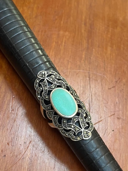 Anel de prata de lei estilo Art Déco, que apresenta uma pedra cabochão oval de turquesa centralizada, envolvida por uma intrincada estrutura vazada totalmente cravejada de marcassitas. Aro 21.