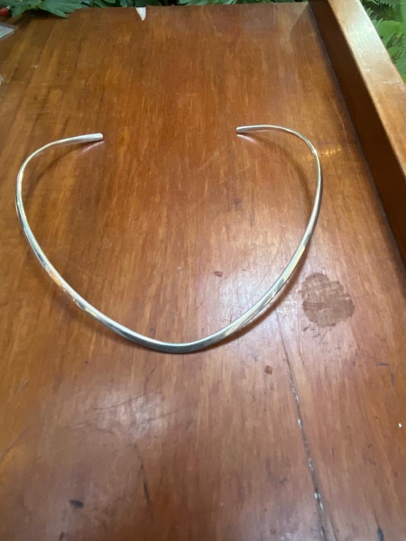Colar de aro rígido (também conhecido popularmente como gargantilha aro ou choker rígido). Este modelo específico apresenta um formato sutil em V ou ovalado na parte frontal, feito de metal polido ger