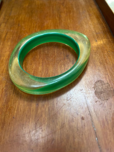 Bracelete rígido vintage (estilo bangle), feito de resina acrílica, apresentando um design translúcido em tom verde com efeito marmorizado ou degradê em amarelo/âmbar. Esse tipo de acessório robusto e