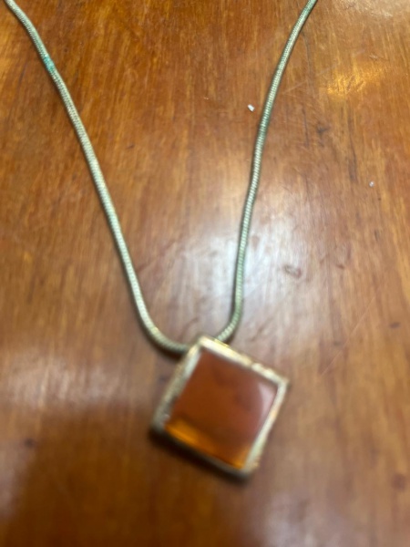 Colar de malha rabo de rato (snake chain) equipado com um pingente quadrado em gema translúcida de tom alaranjado ou caramelo.