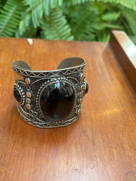 Bracelete rígido de estilo boho tribal, feito em metal prateado com acabamento envelhecido. Pedra Central:possui um grande cabochão oval preto polido ao centro, detalhes em pedra ônix. DetalhesLaterai