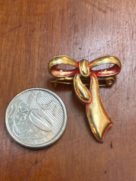 Brochevintage em formato de laço, feito em metal dourado com acabamento esmaltado em tom alaranjado ou avermelhado nas bordas internas.