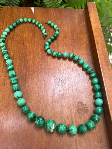 Colar de malaquita natural, caracterizado por suas esferas de tons verdes vibrantes e as marcantes faixas ou veios concêntricos pretos e verde-escuros típicos desse mineral.O design do colar utiliza c