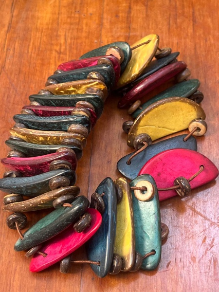 Esta imagem mostra uma pulseira artesanal de estilo boho, feita com fatias ou lascas coloridas de casca de coco