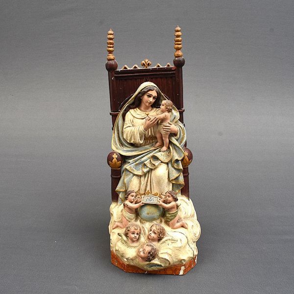 Imagem espanhola representando Sant’Ana entronizada, portando ao colo a imagem de Nossa Senhora ainda menina, em gesto afetuoso. Trono em madeira entalhada. Sant’Ana veste túnica branca com barra dour