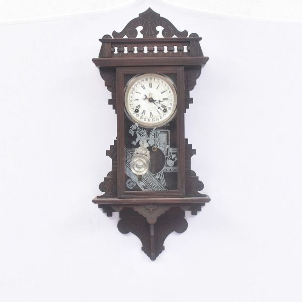 Relógio de parede americano Waterbury Clock Co., de origem norte-americana, confeccionado em madeira ebanizada ricamente entalhada, com caixa ornamentada de inspiração vitoriana, característica do fin