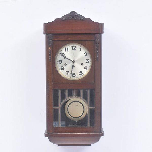 Relógio de parede alemão da primeira metade do século XX da marca Junghans, confeccionado em madeira nobre com acabamento escurecido, apresentando caixa retangular de linhas sóbrias e elegantes. Mostr