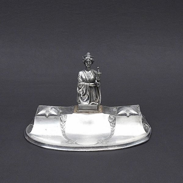 WMF . Tinteiro em pewter, início do século XX, de inspiração Art Nouveau, apresentando base de contornos sinuosos e decoração em relevo com ramos e folhas estilizadas. A composição é coroada por figur