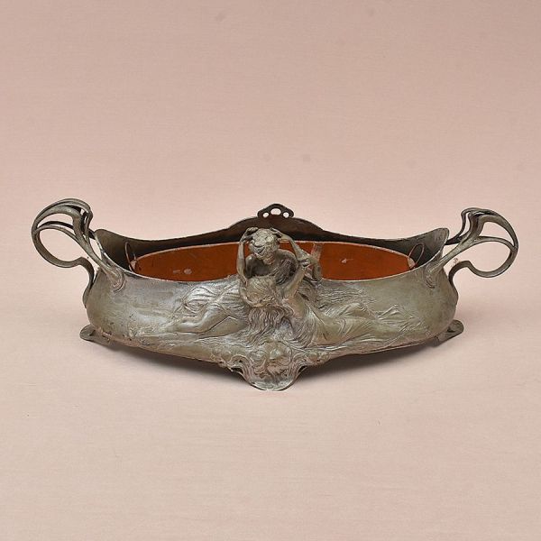 Centro de mesa Art Nouveau em metal (provavelmente estanho ou liga de zamac/peltre) com pátina prateada, apresentando alto-relevo figurativo de ninfa semi-nude com cabelos longos e fluidos, drapeado t