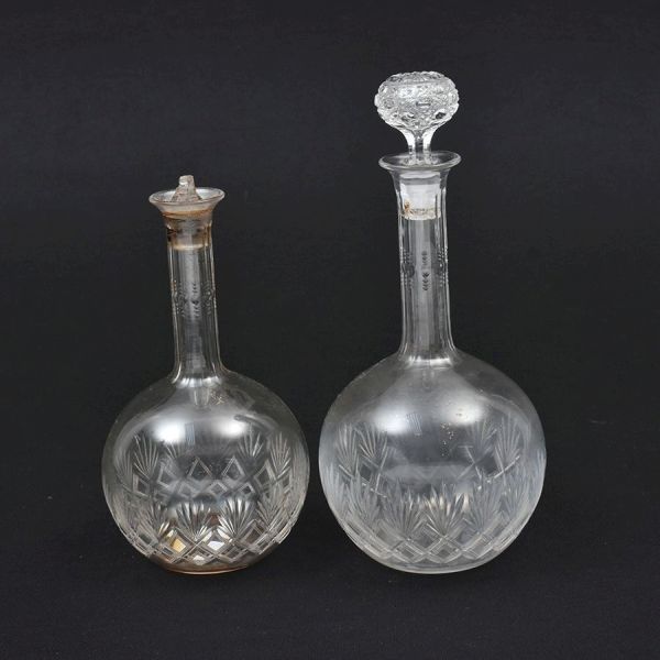 Par de licoreiras francesas em cristal translúcido, ricamente lapidado e gravado com monogramas e motivos geométricos e florais. Corpos globulares com gargalos alongados canelados, evidenciando o refi