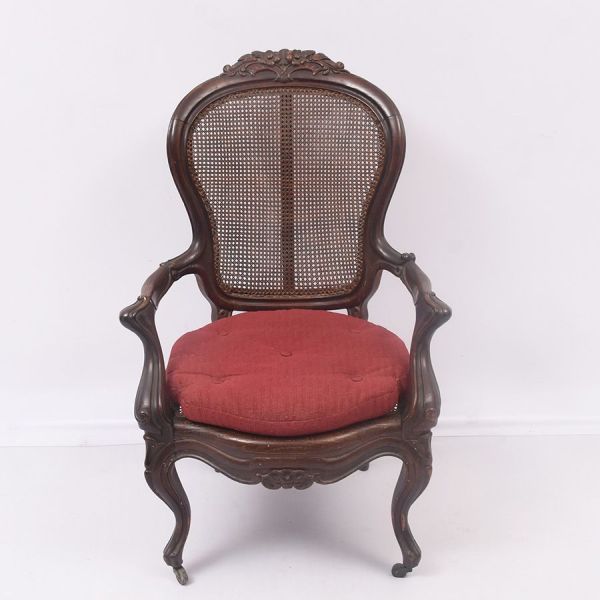 Poltrona em madeira entalhada, em estilo Napoleão III. Espaldar em formato de balão, encimado por crista entalhada com motivo floral, encosto e assento em palhinha original. Braços em dupla voluta com