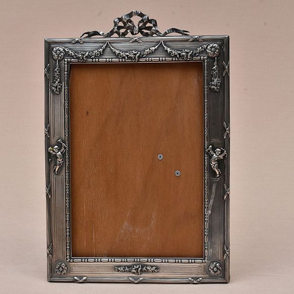 Porta-retrato francês em prata em estilo neoclássico com influências do repertório decorativo do final do século XIX e início do século XX. A moldura apresenta rica ornamentação em relevo, destacando-