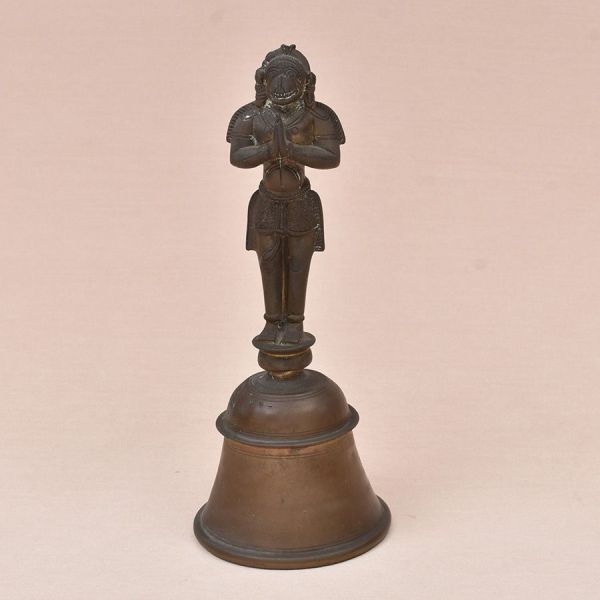 Sineta com cabo em forma de Hanuman. Sineta ritual indiana em bronze fundido, corpo em formato de sino tradicional (côncavo, com bordas em friso de linhas concêntricas), encimada por cabo escultórico