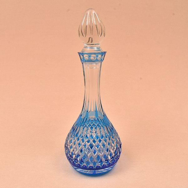 Baccarat. Licoreira em cristal lapidado, em corpo bojudo com base circular, gargalo estreito canelado e tampa em formato de gota facetada. O cristal apresenta coloração azul degradê — mais intensa na