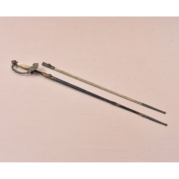 Espada do Império do Brasil. Guarda vazada em metal ricamente cinzelado e ornamentação floral. Destaca-se pela presença do Brasão Imperial Brasileiro. Empunhadura em madrepérola natural, elegantemente