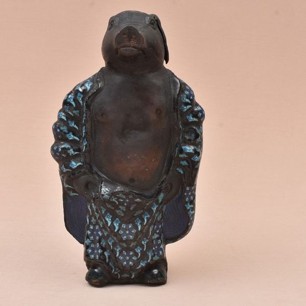 Escultura chinesa de porco antropomorfizado em ferro patinado com esmalte cloisonné. Figura encontra-se de pé, representando porco em vestes talares, associada ao signo do zodíaco chinês. Corpo e cabe